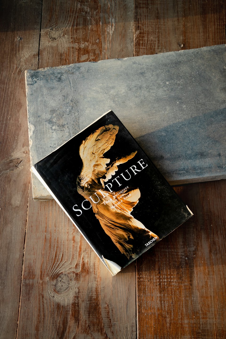 An art book rests on concrete atop a wooden table.